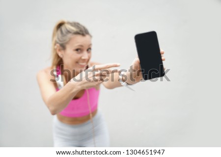 Smiling woman in sporstwear pointing to cellphone on white background