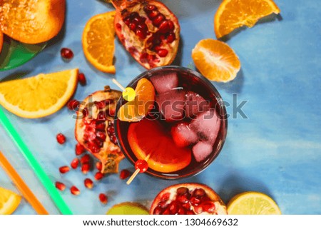 Pomegranate juice in a glass with pieces of ice on the background of cut citrus fruits.