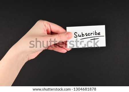 Subscribe text on a card in woman hand  on a black background.