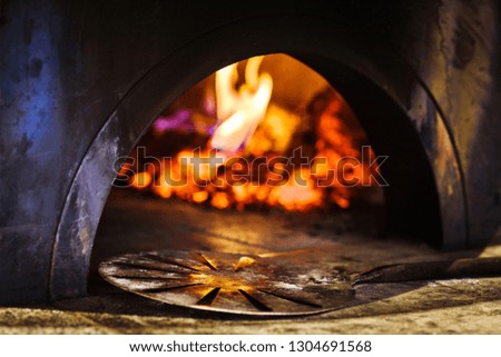 Shovel in front of burning wood and flames in fireplace of ready to use traditional italian brick pizza oven