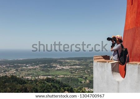 Young woman photographer taking picture of portuguese landscape from castle tower