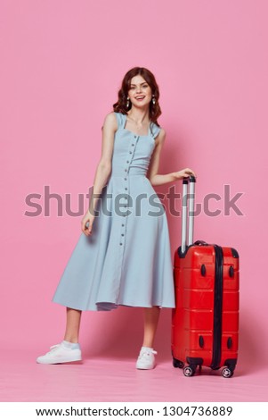 A woman in a sundress sneaker holds a suitcase on a pink background                 