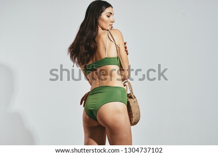 A woman in a green swimsuit cropped view bag in hand                   