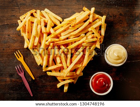 Heart shaped serving of French Fries with dips, dressings or sauce in small bowls alongside on wood Royalty-Free Stock Photo #1304748196