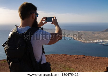 The man photographs an island in the ocean, standing on the edge of a cliff.