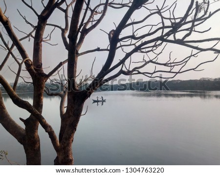 Perfect Picture of lake, where the shun is about to set and fisher is in his boat for fishing. Pic was take from the bank of pond with the angel of a tree which has no leaf. 