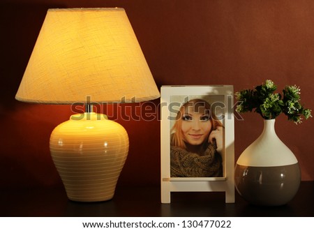 White photo frame and lamp on wooden table on brown wall background