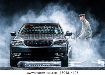 A car washer washes a gray car with a high-pressure washer at night on the street. Expensive advertising photography
