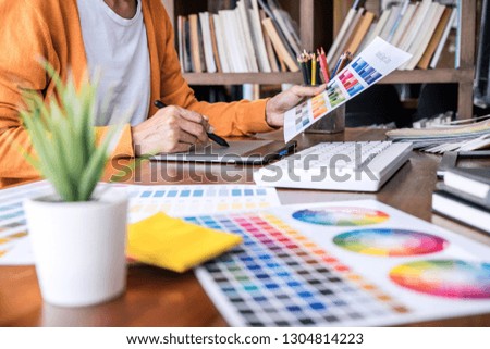 Image of female creative graphic designer working on color selection and drawing on graphics tablet at workplace with work tools and accessories.