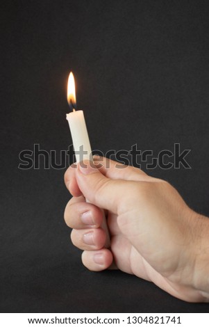 A hand holding a candle on black background