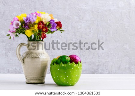 Bouquet of colorful freesia flowers in ceramic vase and Easter eggs. Copy space, background, wallpaper, cover art. 