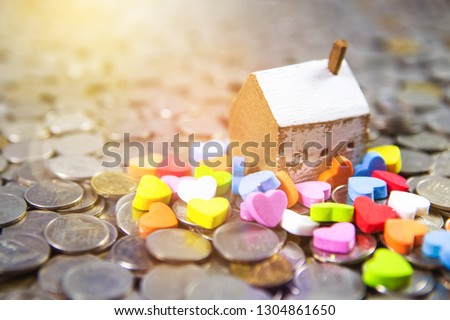 Wooden house model and colorful multi-color of heart icon on a pile of coins. Home sweet home or love in family concept with copy space.