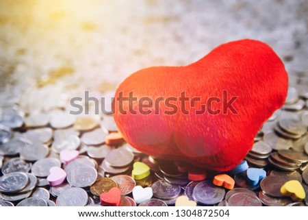 Red heart icon and small colorful heart on pile of coins. Home sweet home or love in family concept with copy space.