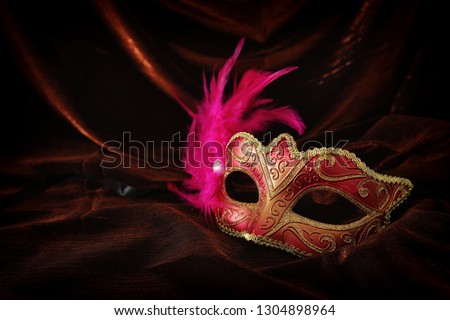 Photo of elegant and delicate gold, red venetian mask over dark velvet and silk background