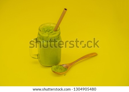 Green tea latte with ice in mason jar and straw and spoon with powder matcha on yellow background. Homemade Iced Matcha Latte Tea with Milk zero waste