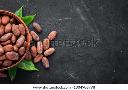 Cocoa beans in a bowl on a black background. Top view. Free copy space.