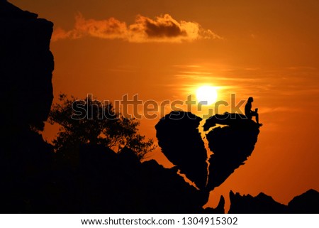 woman on the broken heart shape rock on the mountain with red sky sunset.Silhouette Valentine background concept.