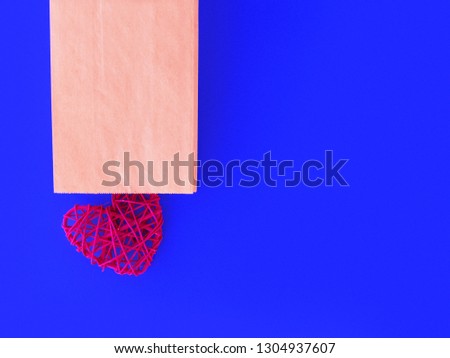Red wicker heart shape is in an open paper bag or envelope on a blue background.
