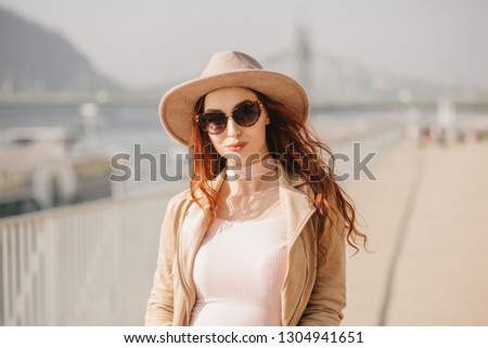 Outdoor photo of smiling winsome lady with long wavy hair. Interested ginger girl in hat posing on blur nature background.