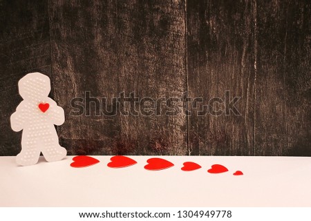Plastic figure of a man with a red heart. Red cardboard hearts are arranged in a row. Dark wooden background. concept of love. Valentine's day. Copy Space.