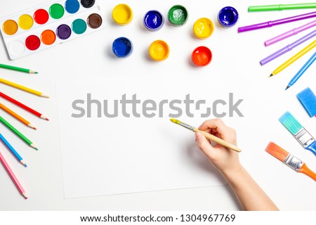 Kid hands start painting at the table with art supplies, top view Royalty-Free Stock Photo #1304967769