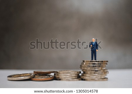 Miniature people, businessman show good job symbol standing on pile coins using as business and financial concept