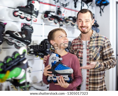 Father and boy boasting purchased roller-skates in sports store