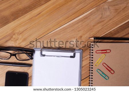 Working place on wooden table. Office desk table with eye glasses notebook, office plant, pen ,clips,and smartphone. Top view with copy space, flat lay