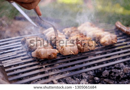 Barbecue in nature.
Preparing food at picnic.Chicken drums and sausages grilled on burning charcoal.