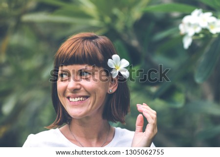 Portrait of pretty young woman with frangipani plumeria in the ear on the beautiful green background. Bali island vacations.