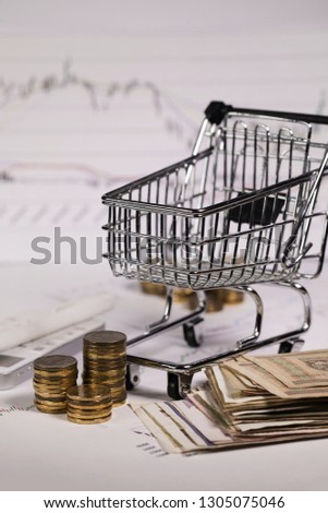 Small shopping cart on stock market charts. Coins in the background