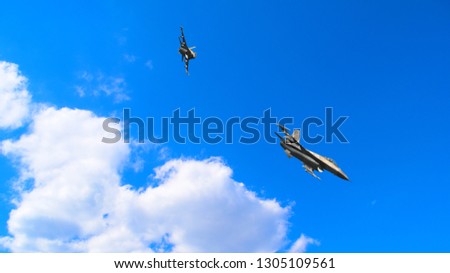 Two military aircraft flying against the blue sky near the white clouds

