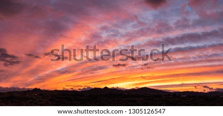 Two image panorama of colorful streaks of clouds at sunrise with the silhouette of hills below. 