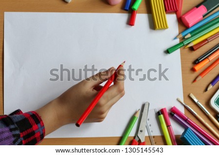 Top view on table with blank sheet of paper and baby's hand with pencil. Back to school. Color paints with paint brushes, pencils and plasticine. Kids painting concept. Children art. Top view