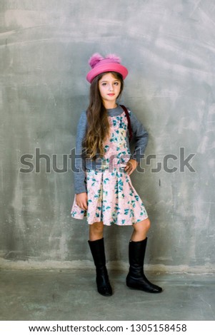 Charming cute little girl with long brunette hair in dark blue dress expressing isolated on grey background standing by putting her hands on an old wooden sewing machine
