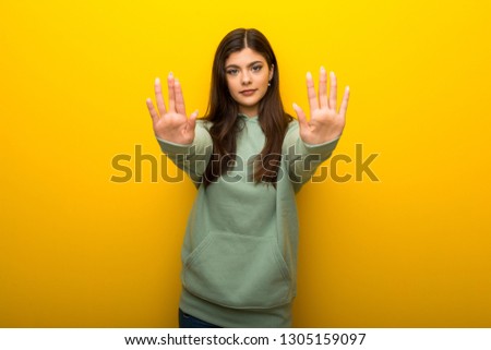 Teenager girl with green sweatshirt on yellow background making stop gesture for disappointed with an opinion