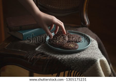 Chocolate cookies on the plate. Dark and Moody, Mystic Light food photography. Children's hand takes a cookie from the plate.