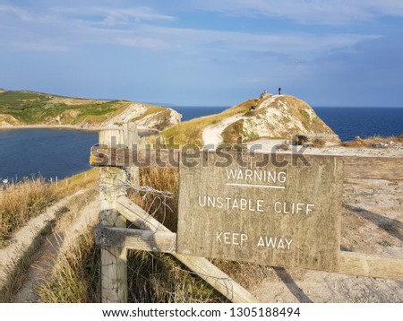 Photo of a cliffside view at Lulworth cove with a hazard warning sign.