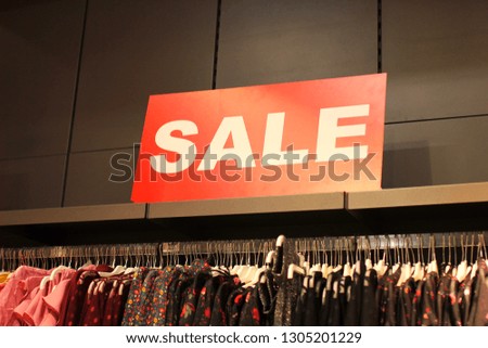 Sign with text "Sale" and lots of shirts below on hangers  in the clothes store