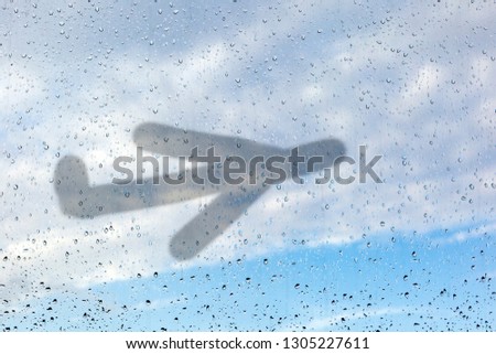 Picture of an airplane on misted glass. A window glass with raindrops against a blue sky. The concept of non-flying weather, flight delay.