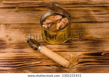 Can opener and tin can with sardine on rustic wooden table