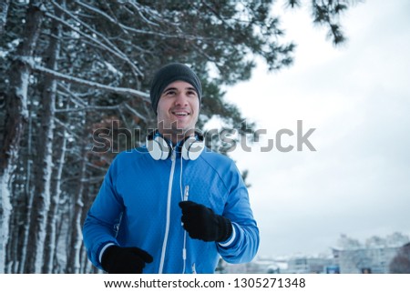 Running on the snow. Young athlete workout in city park and smiles.