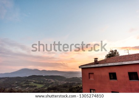 Chiusi sunset evening in Umbria, Italy with red house on mountain countryside rolling hills and colorful picturesque city and sunlight clouds