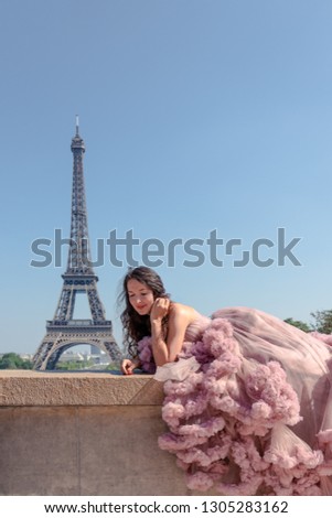 Beautiful hipster girl dressed to impress in a pastel pink ballroom dress with Eiffel Tower in background