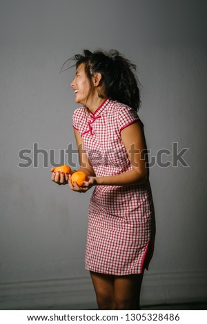 Portrait of a young and attractive Chinese Asian teenage girl in a traditional Chinese dress (qipao) smiling as she offers a pair of Mandarins to signify wealth to the host that she is visiting. 