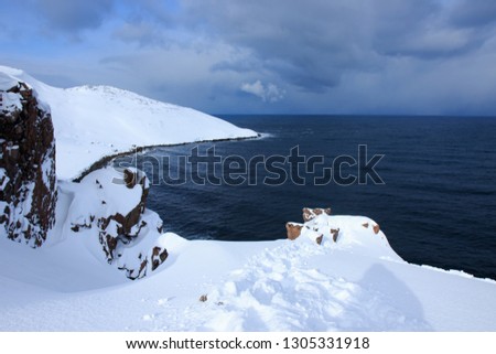 Russian Arctic View, North. Sky with clouds and blue sky reflection in water with waves and snow mountains background with stones grass foreground. Picturesque landscape view, nature scenery beauty