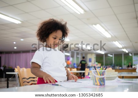 Mixed race girl, tanned skin, Curly short hair sitting, drawing and painting with concentration and intended in the library at school. In Bangkok, Thailand. Education Concept with Copy space