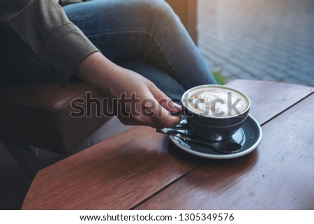 Closeup image of a woman's hand holding and drinking hot latte coffee while sitting in cafe