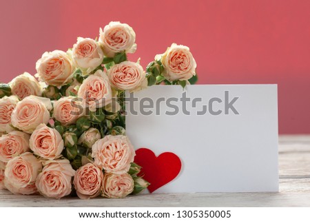 Pink roses flowers with gift card and red paper heart on pink background. Space for text. Holiday concept.
