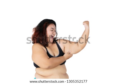 Picture of obese woman looks sad while showing her flabby bicep in the studio, isolated on white background